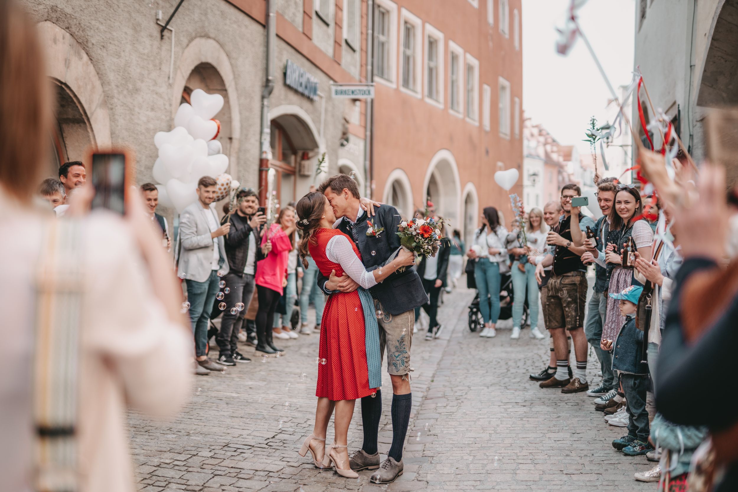 A couple in traditional Bavarian dress dancing on a cobblestone street surrounded by onlookers.