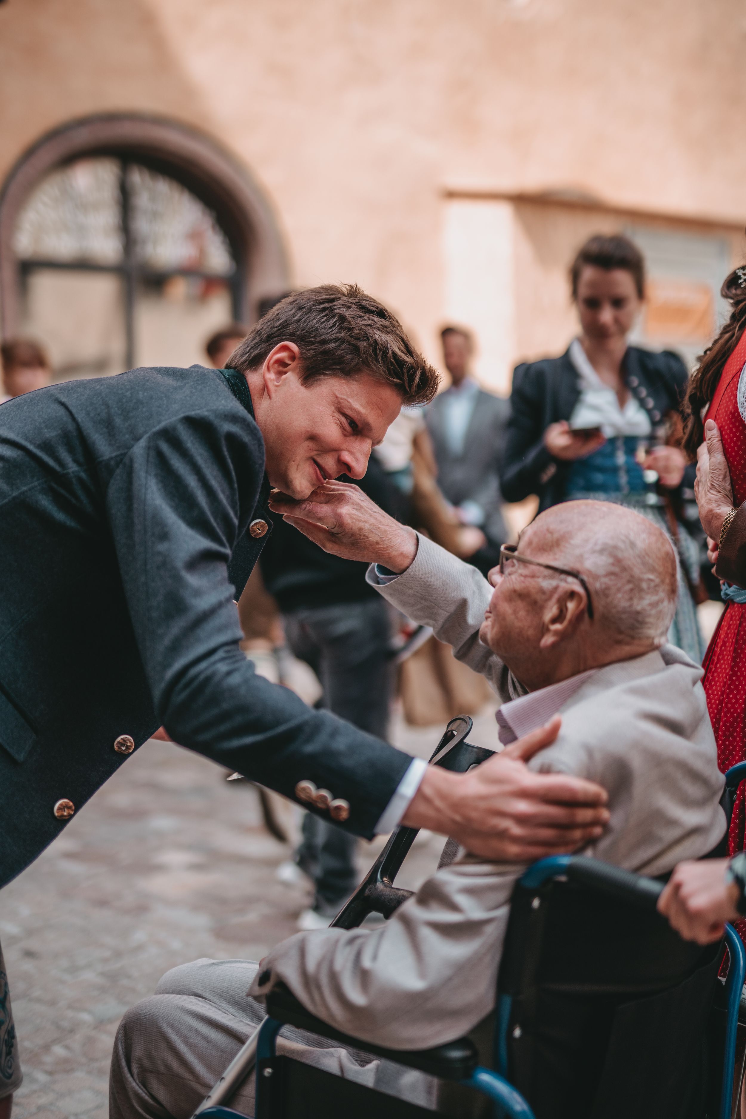 A touching moment between a young man and elderly person in a wheelchair at a traditional gathering.