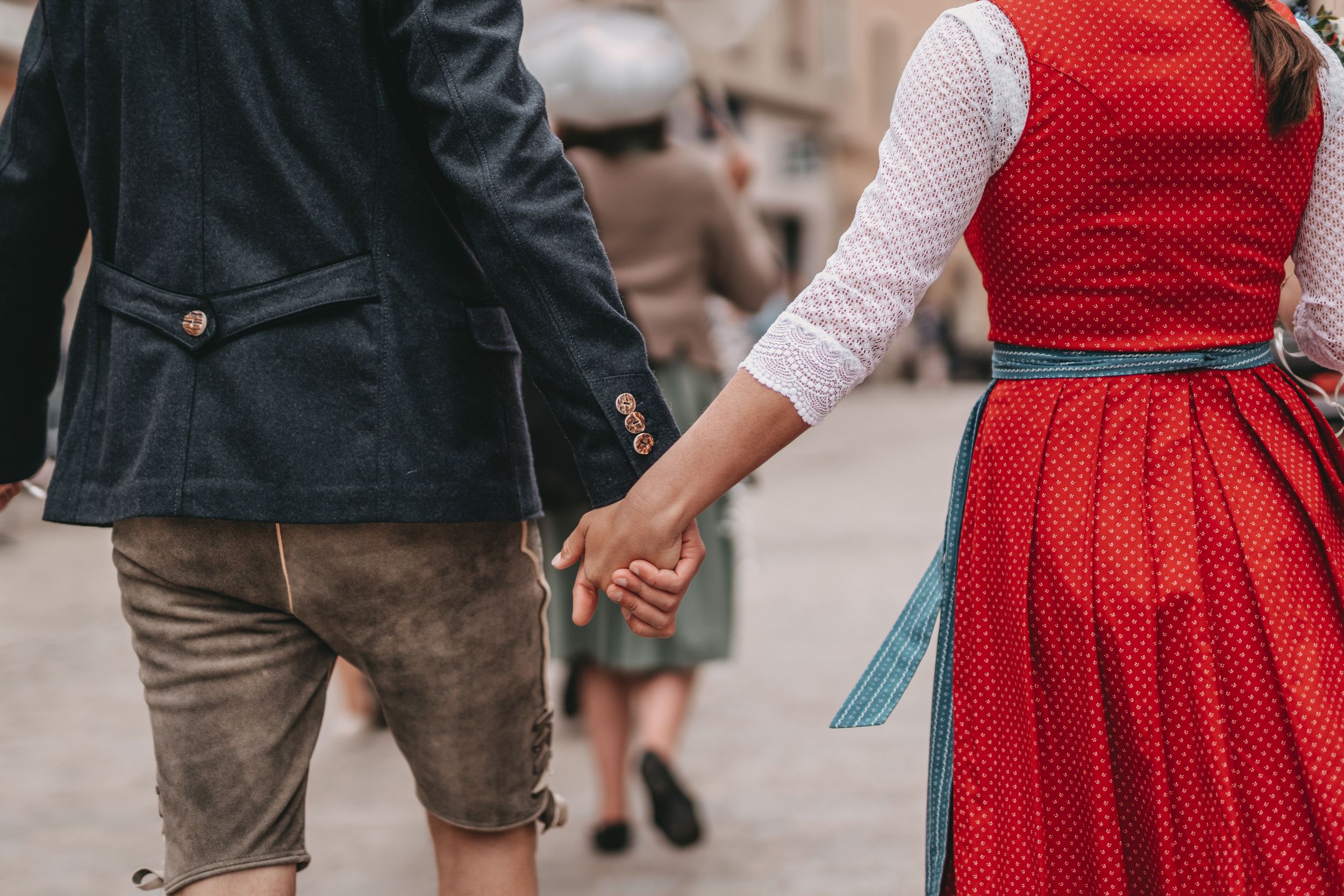 Close-up of couple holding hands while wearing traditional Bavarian dirndl and lederhosen.