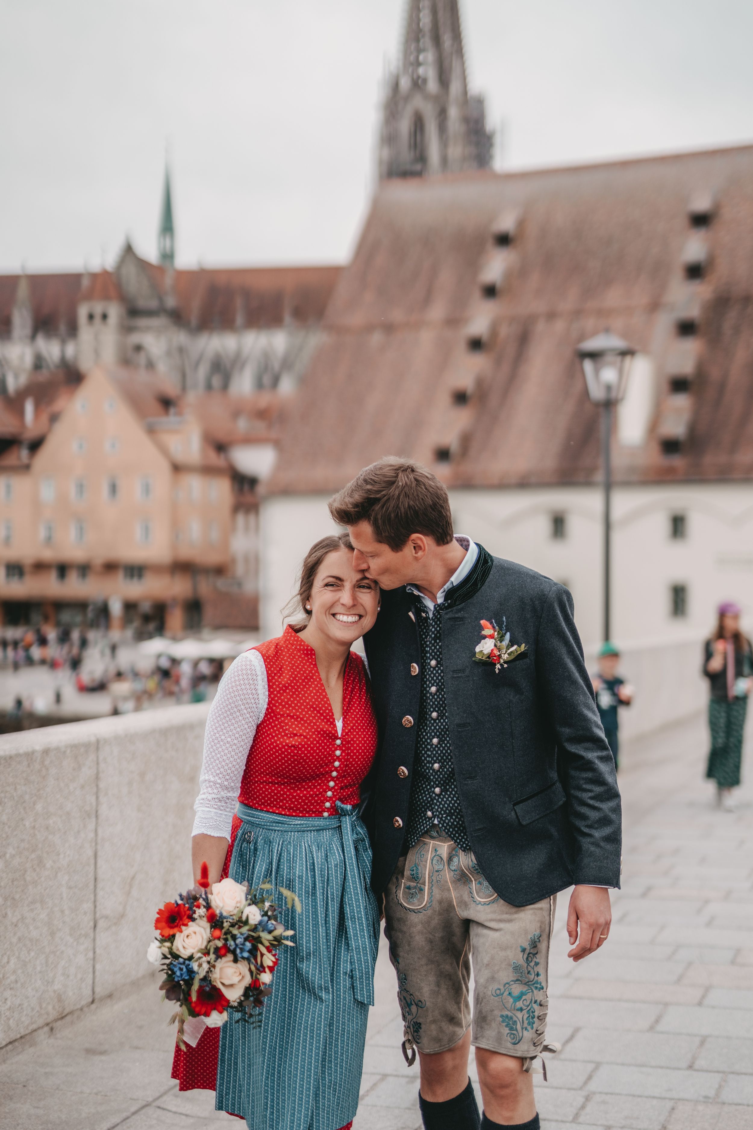 Couple in traditional dress sharing an intimate moment with historic church spires in background.