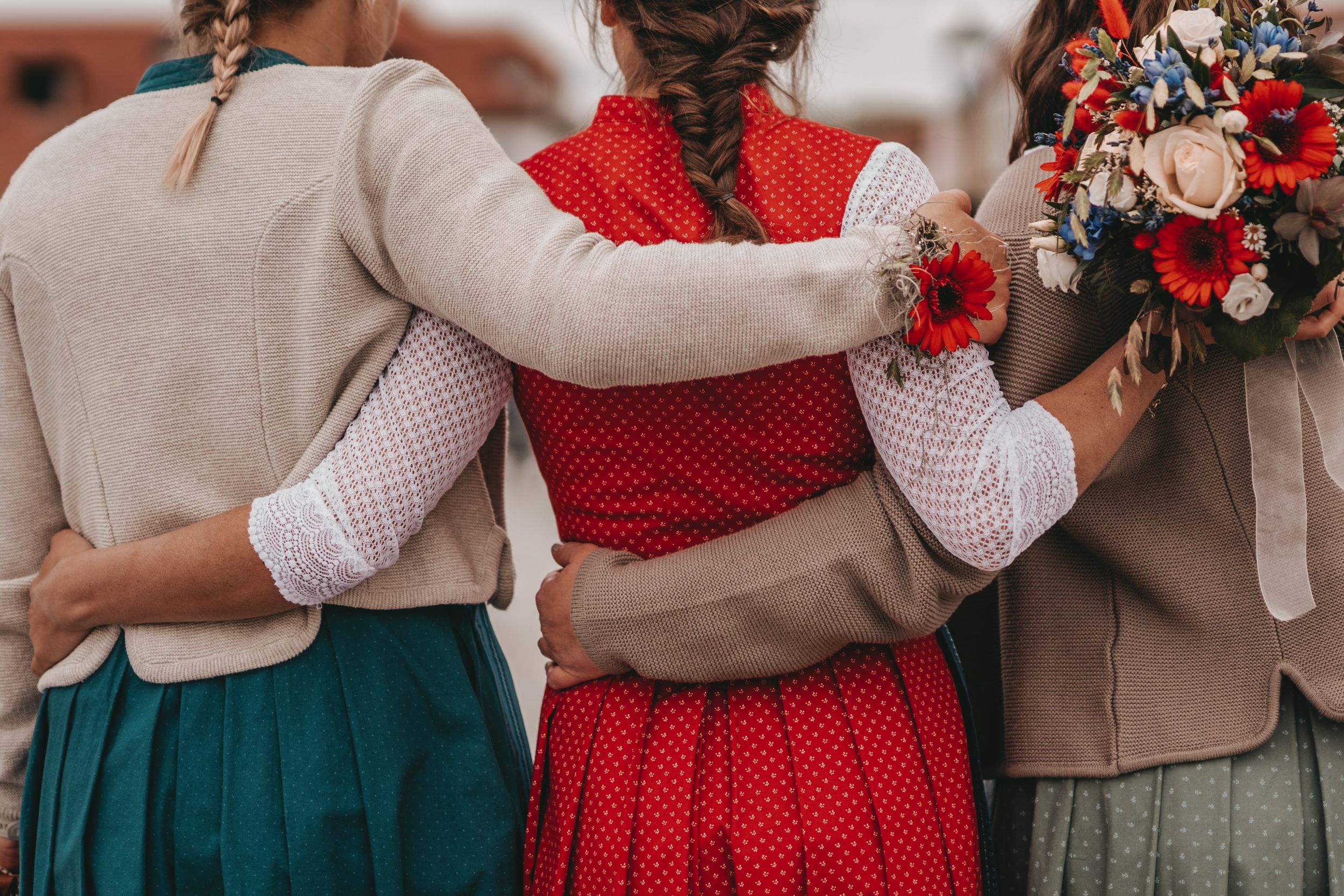 Three women in traditional dirndls embracing in a group hug from behind.