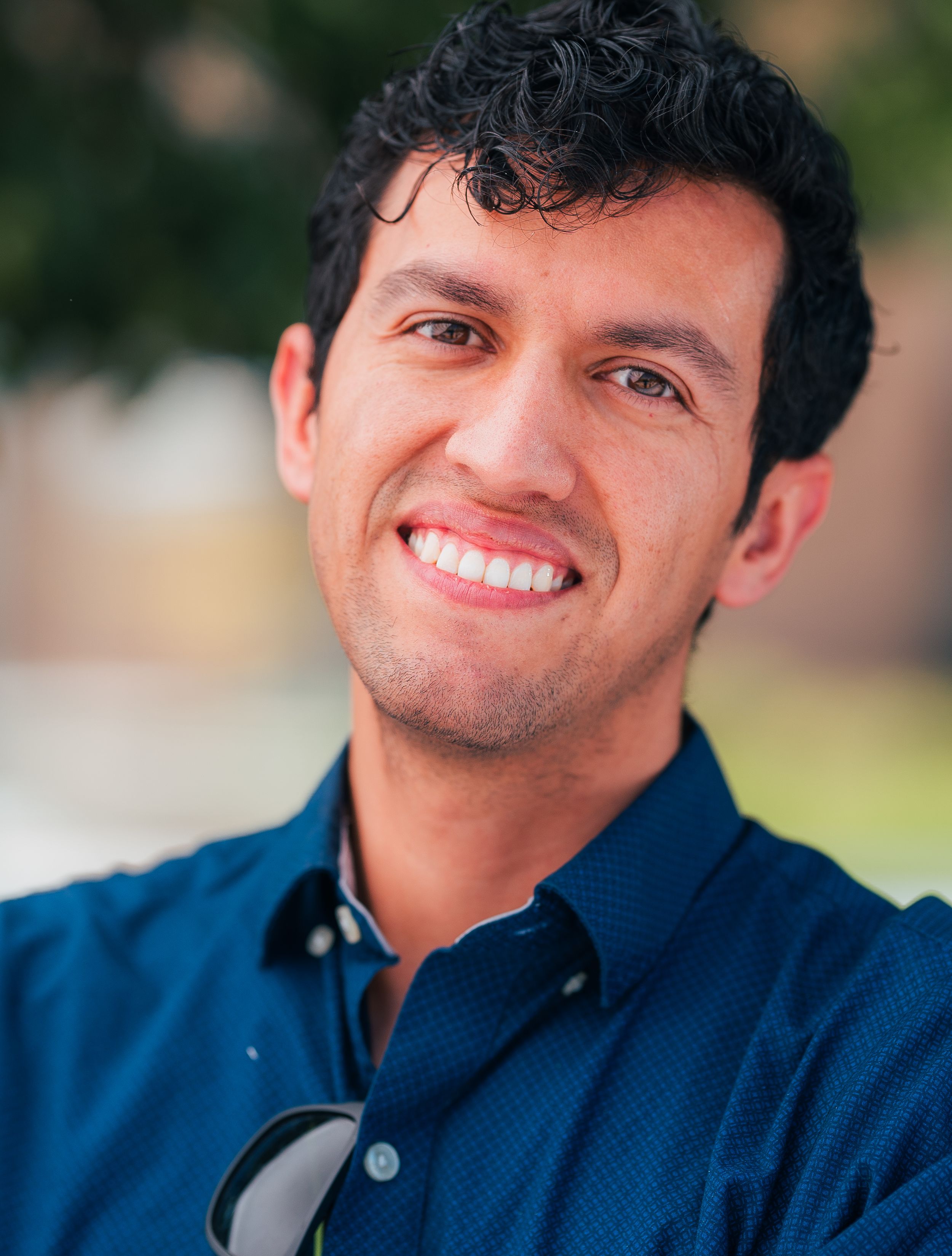 Professional headshot of a person wearing a navy blue button-down shirt with a bright smile.