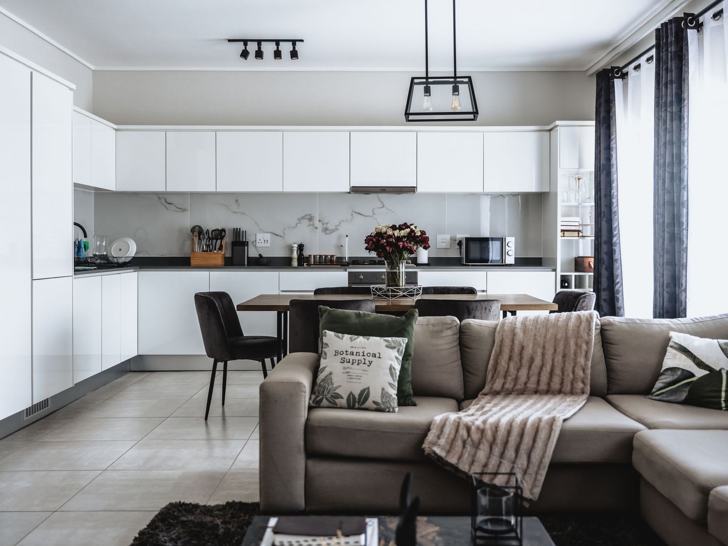 Modern open concept living room with white kitchen and gray sectional sofa.