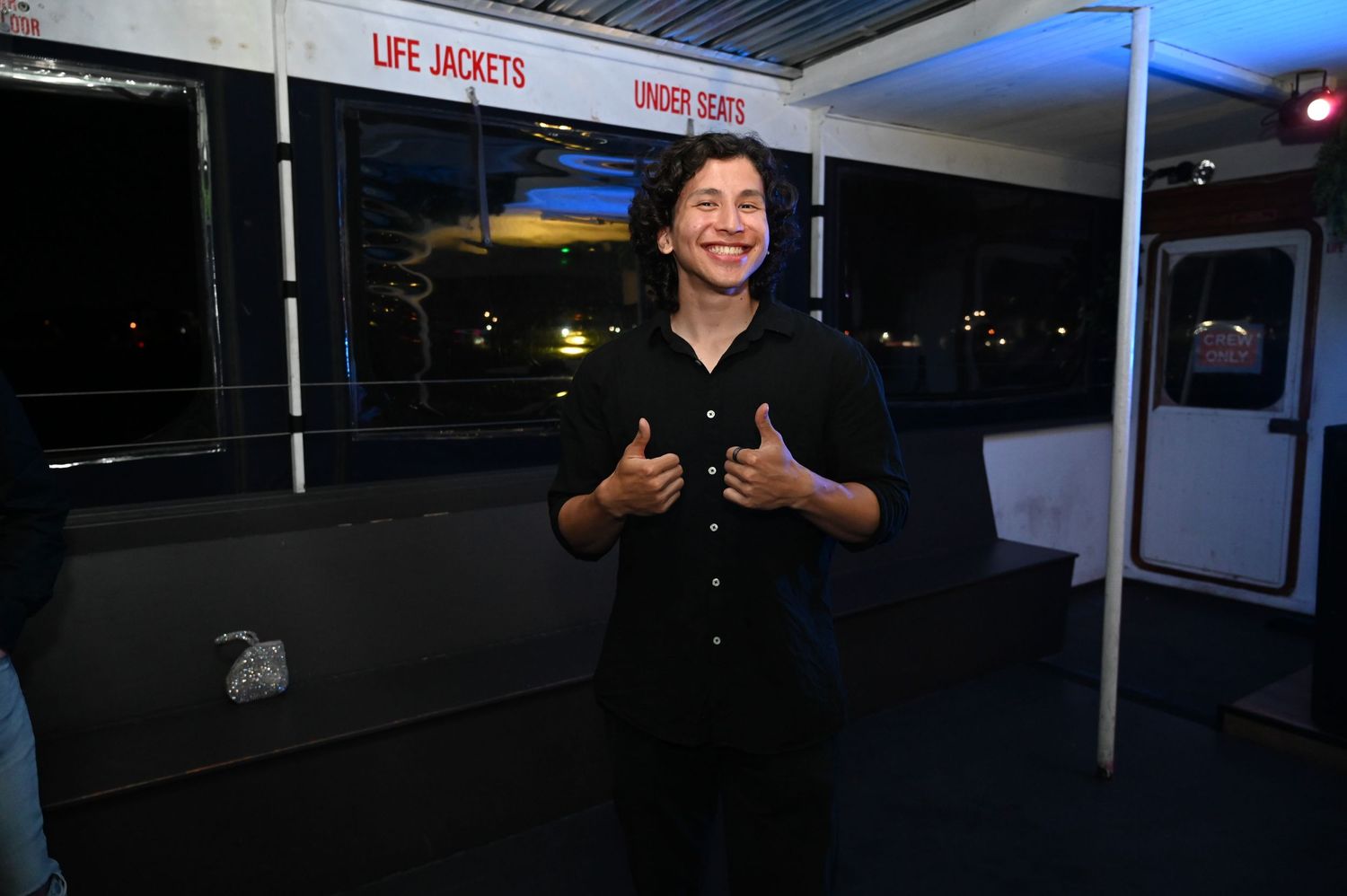 Person gives thumbs up while standing in front of a life jacket storage area at night.