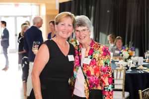 Two attendees pose together at a formal event with decorated tables in the background.