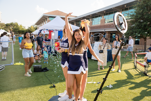 Cheerleaders perform routines on a sunny outdoor lawn during an event.