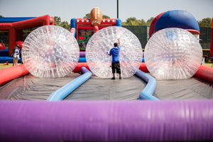Large inflatable zorb balls set up on colorful bounce course at outdoor event.