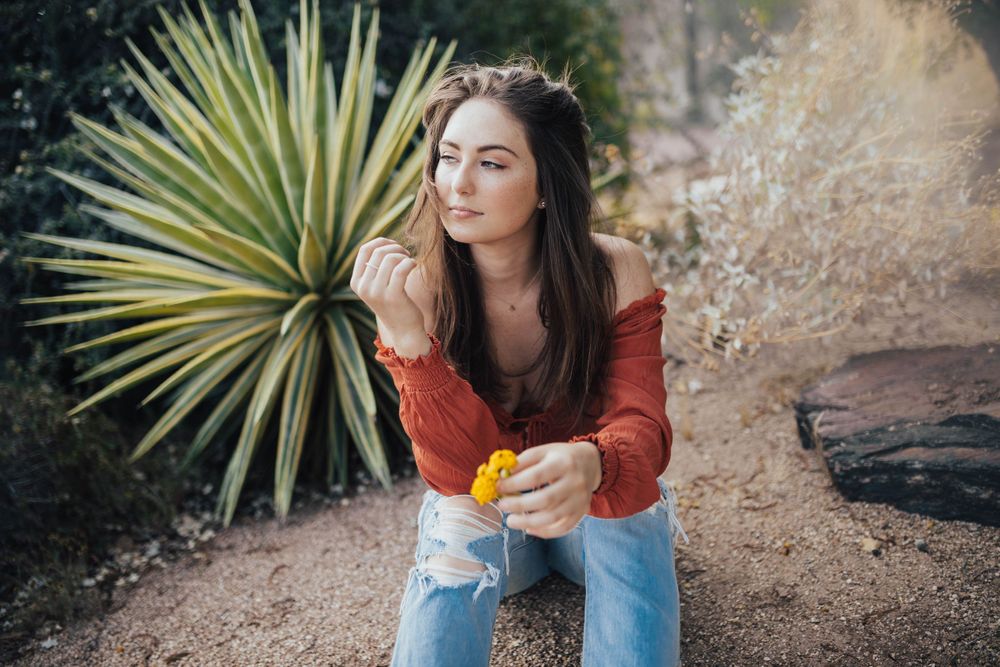 Someone poses thoughtfully near desert plants wearing casual attire in golden sunlight.