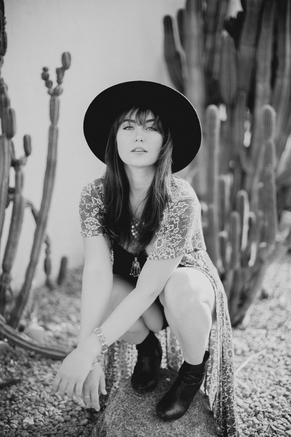 Monochrome fashion portraits with wide-brimmed hat and floral dress in desert setting.