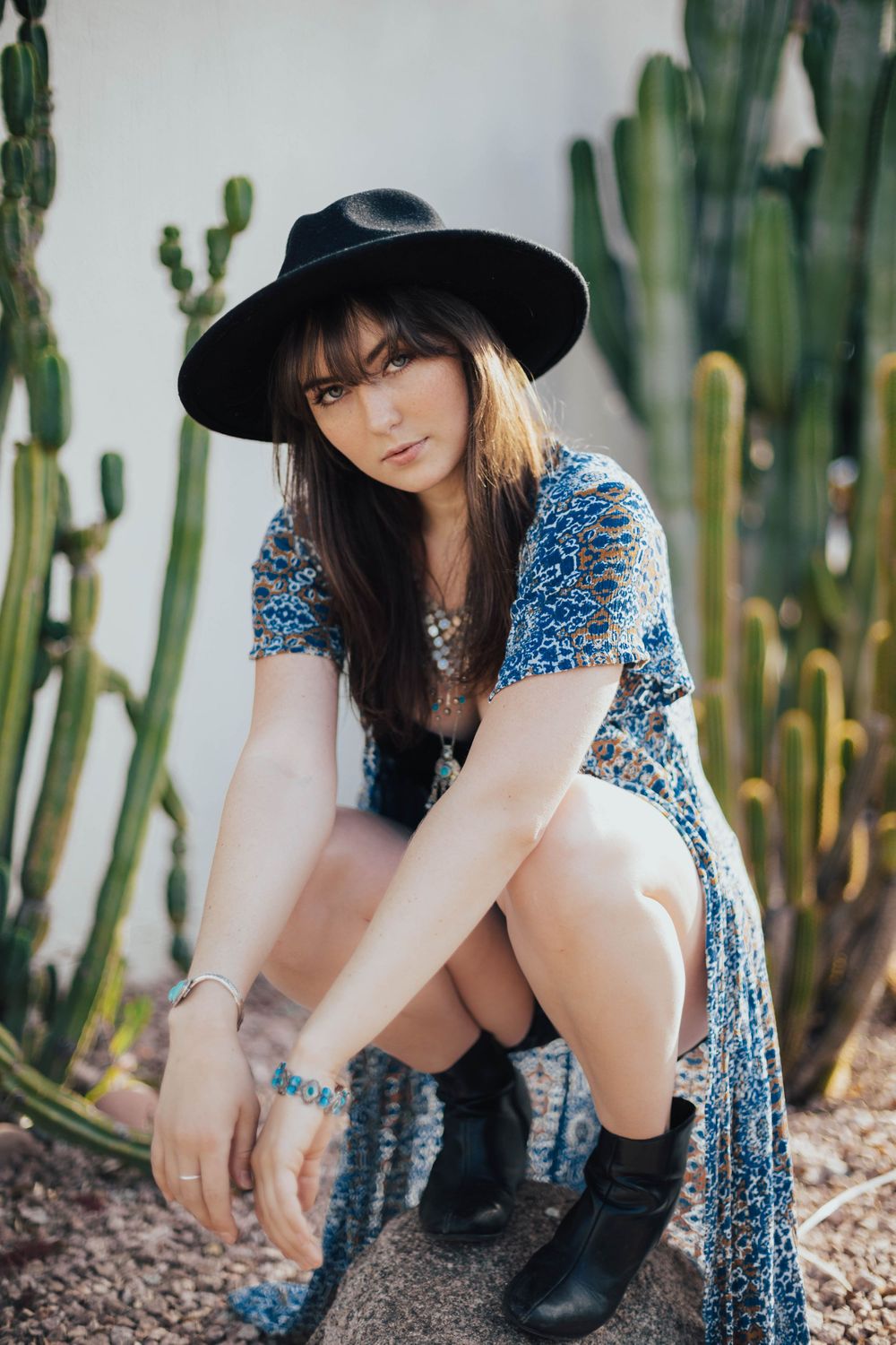 Casual fashion shoot with blue dress and boots among desert cacti and rocks.