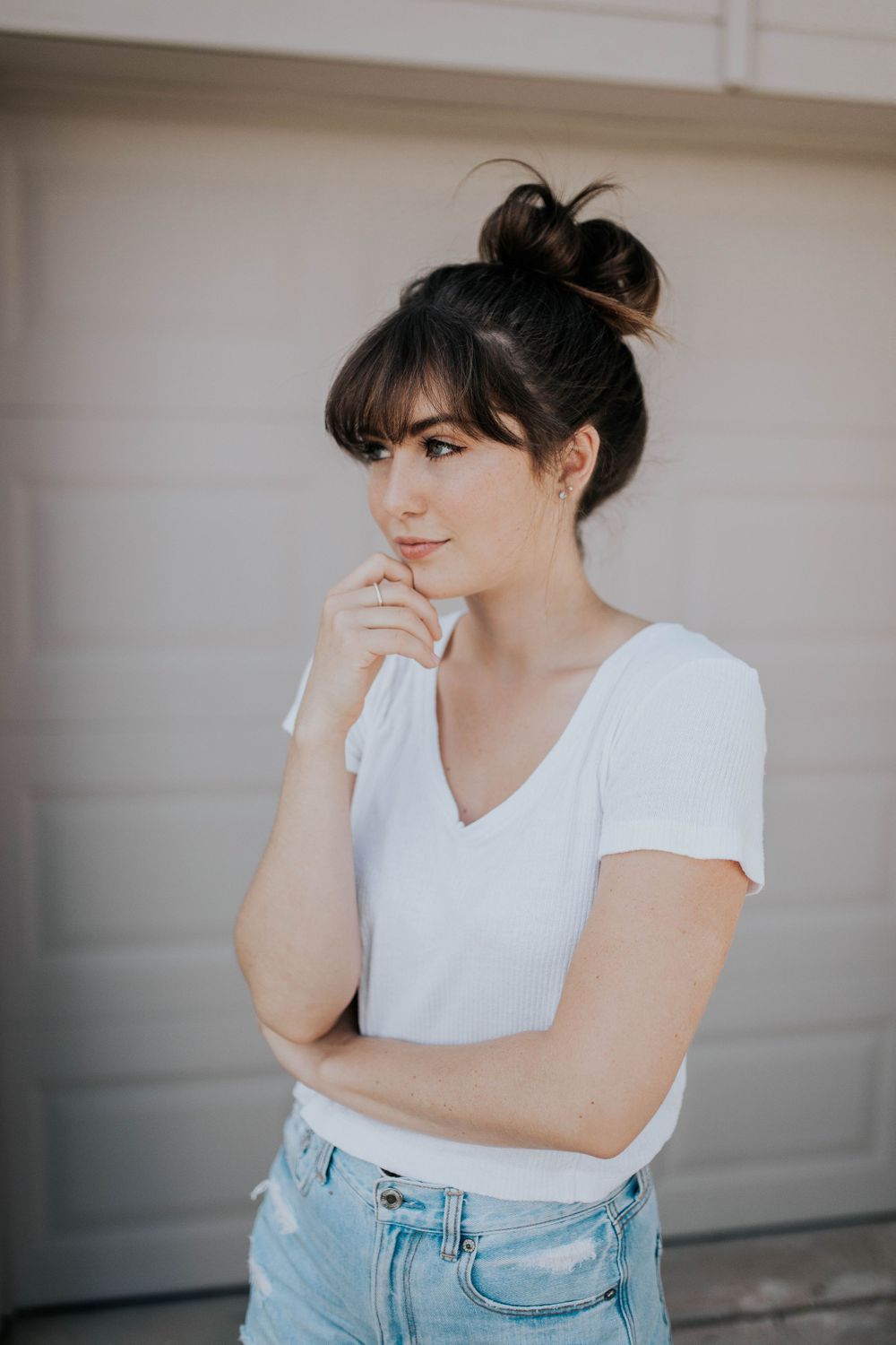 Casual portrait against white garage door wearing white t-shirt and light denim.