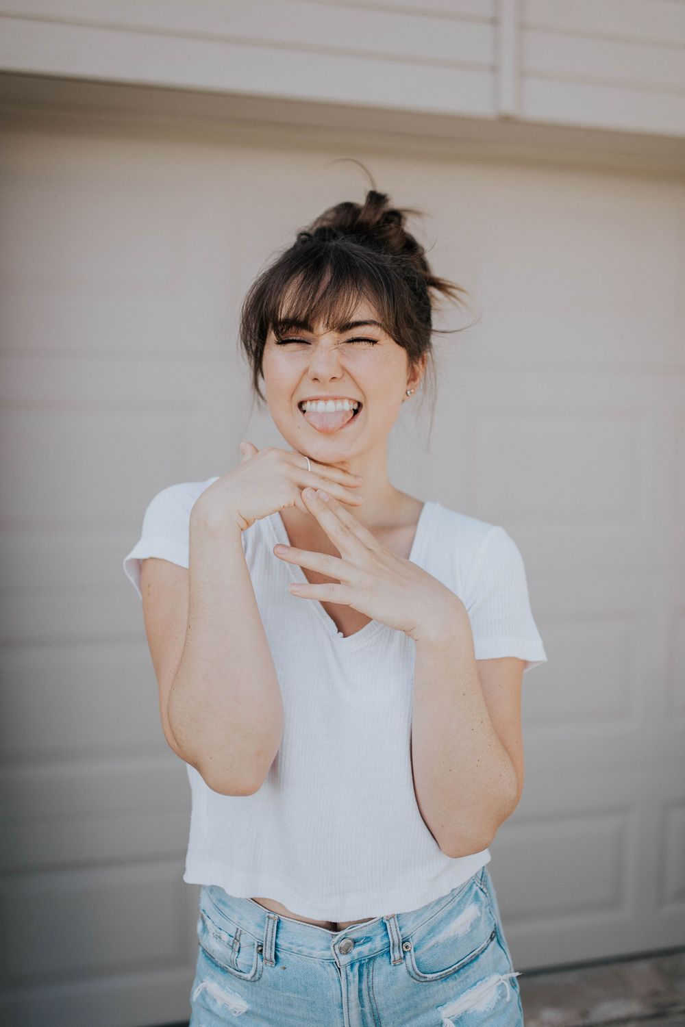 Candid laughing portrait against white garage door in casual white tee and jeans.
