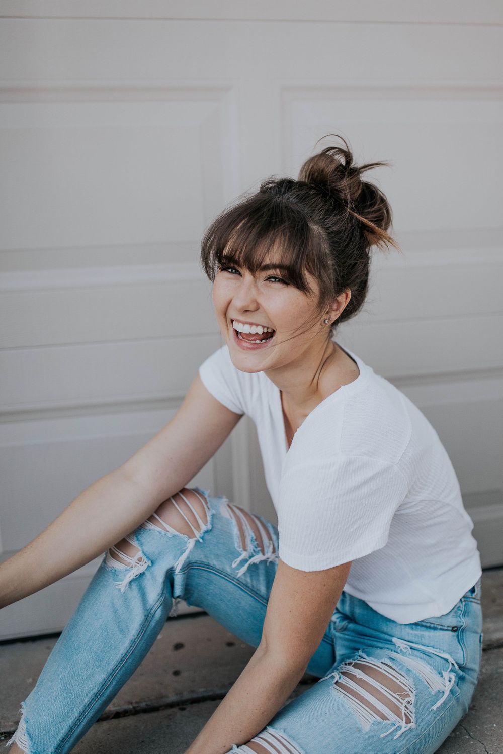 Playful sitting pose against white garage door in casual summer outfit.