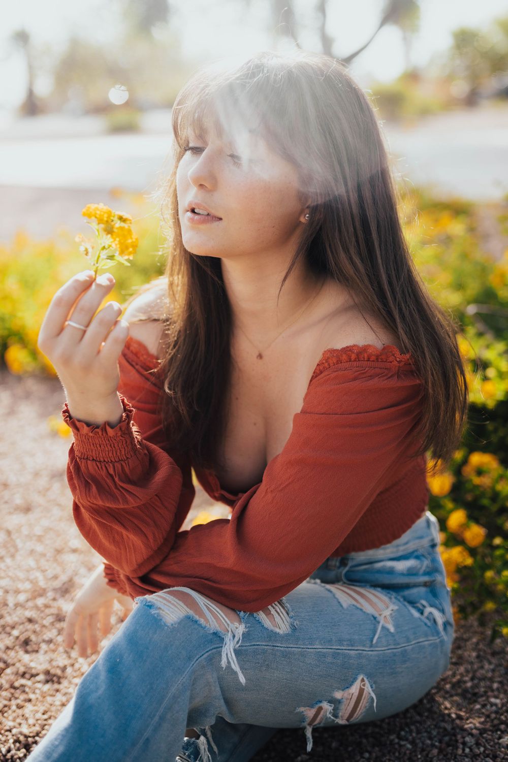 A casual portrait in a garden featuring distressed denim and a rust-colored top among yellow flowers.