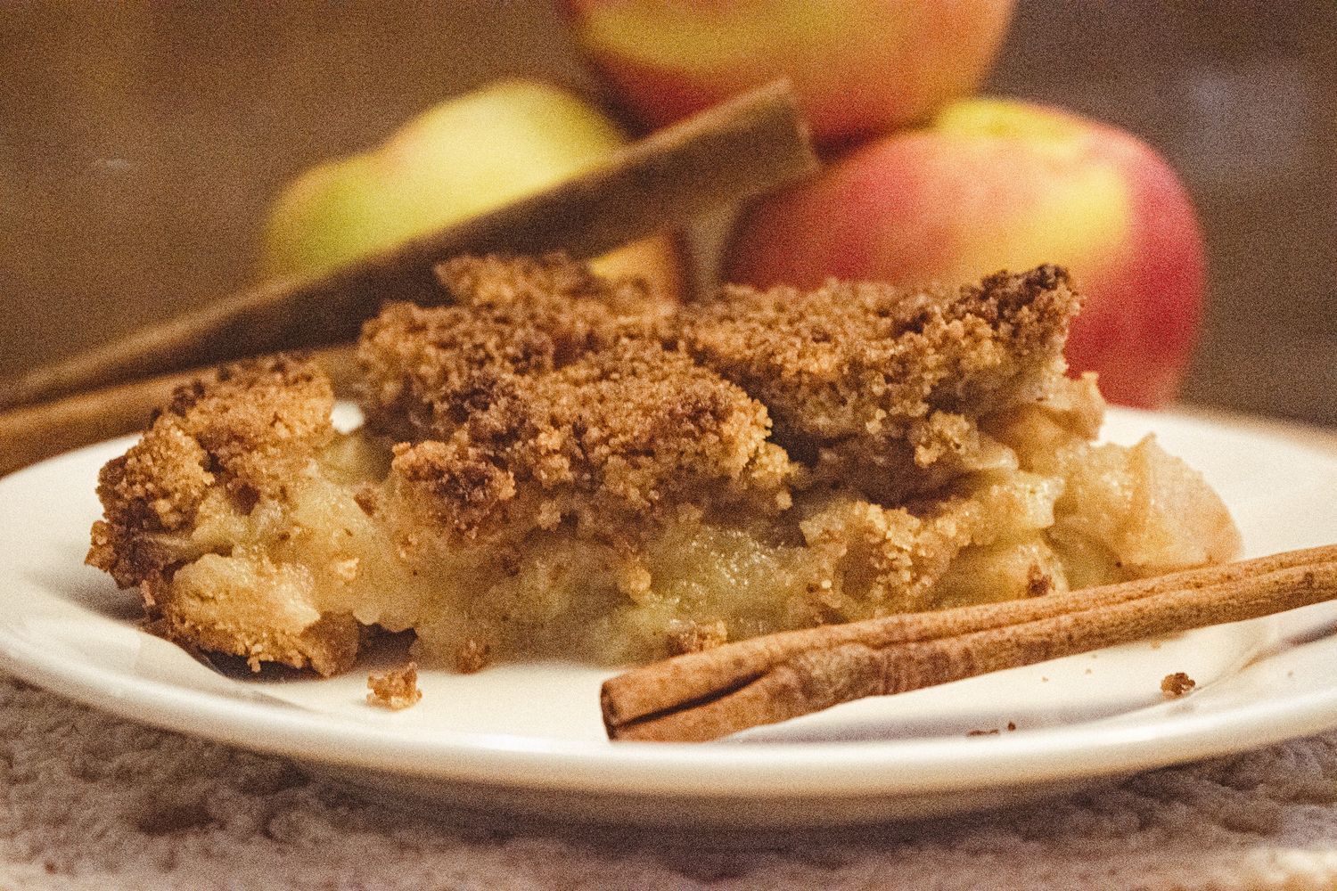 Apple crumble dessert with cinnamon sticks served on a white plate.