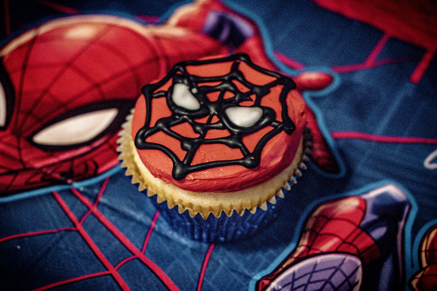 Spider web decorated cupcake on Spider-Man themed background.