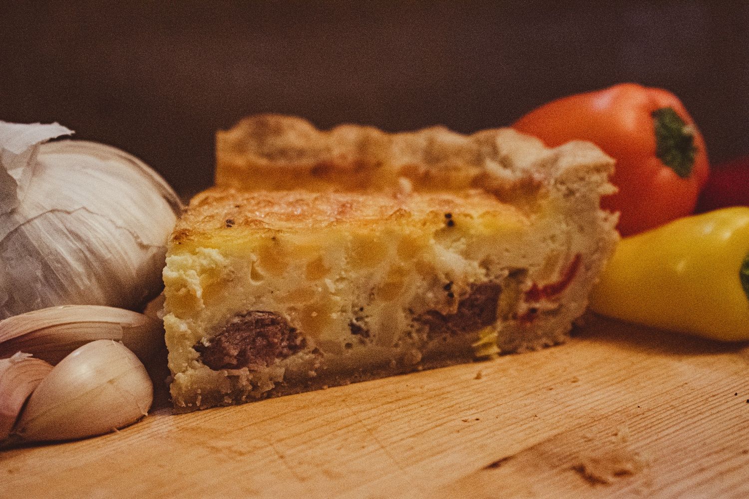 Close-up of a savory quiche with vegetables and garlic on wooden cutting board.