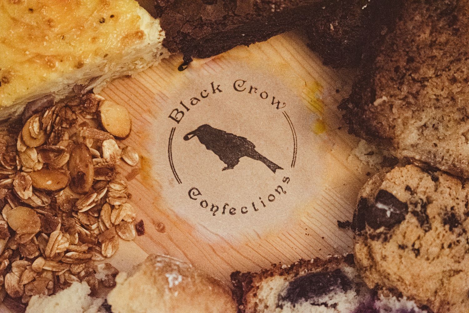 Black Crow Confections logo on wooden surface surrounded by baked goods.