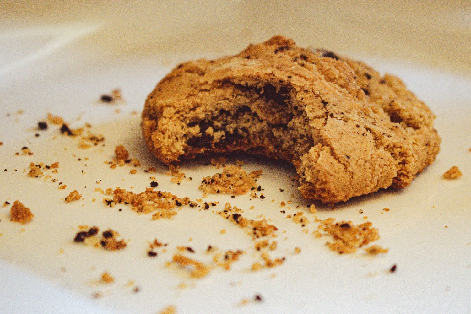 Bitten chocolate chip cookie with crumbs on white plate.