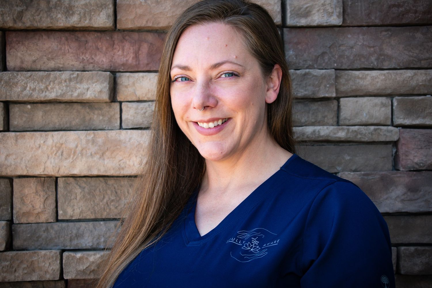 A healthcare professional in a navy blue uniform stands in front of a stone wall.