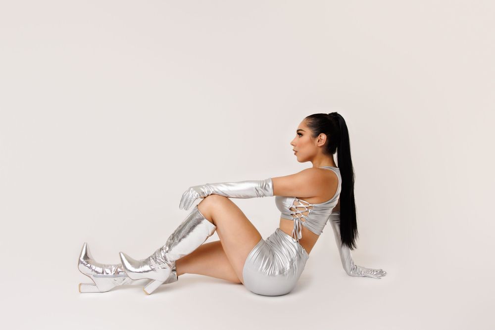Model in silver activewear lounges on white studio floor.