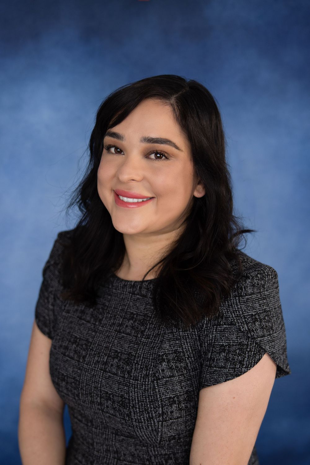Professional portrait series against blue backdrop wearing black textured top.