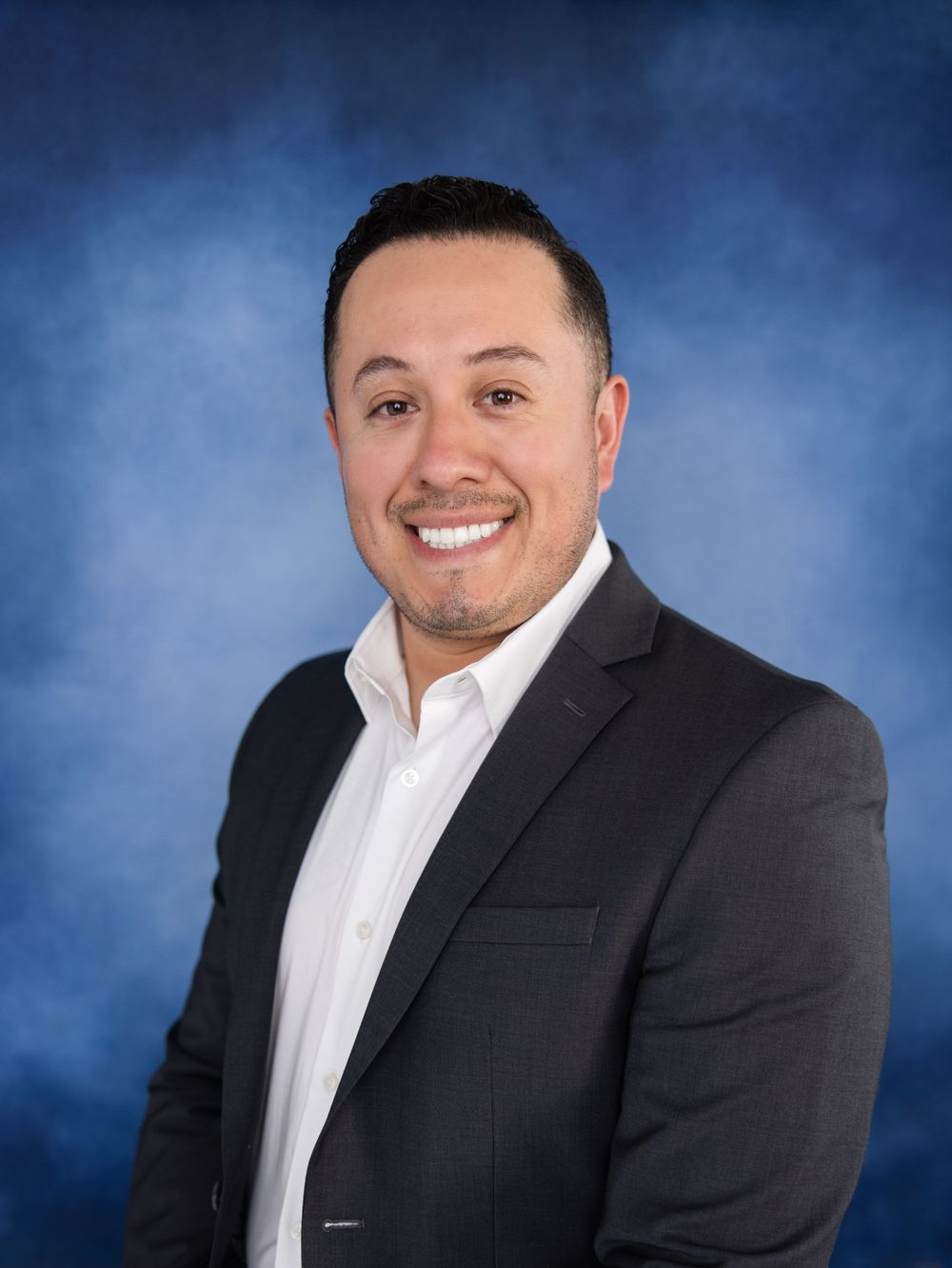 Professional headshot of person in dark suit against blue backdrop.