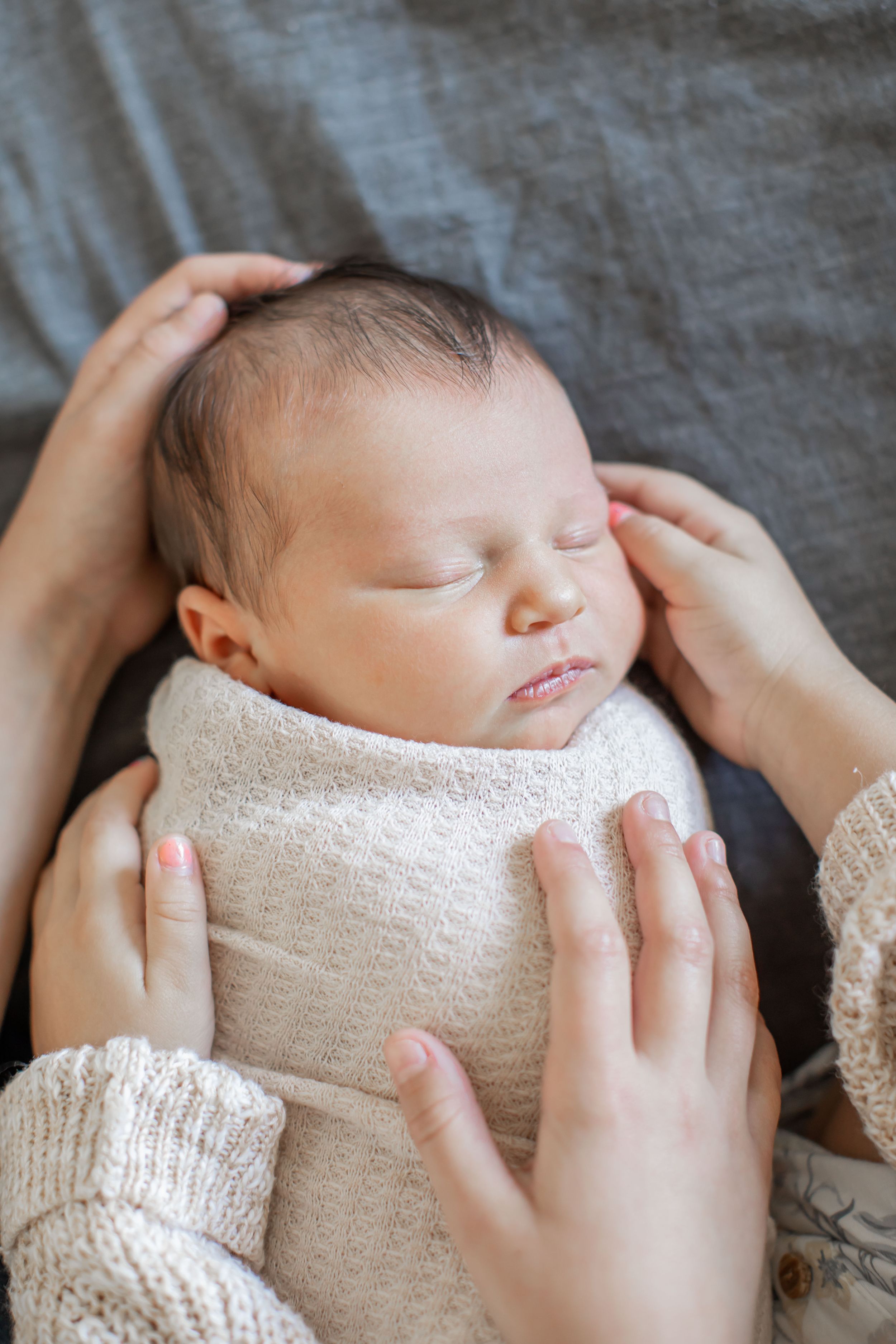 Portrait of a newborn with her two sisters hands cradling her from both sides