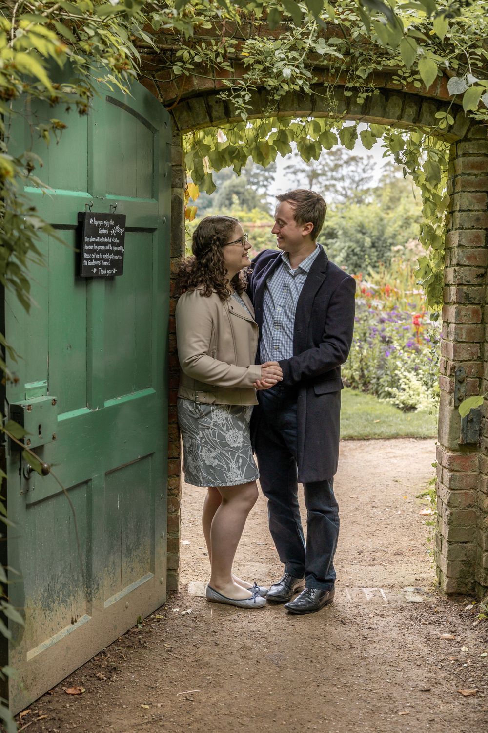 A couple shares an intimate moment under a vine-covered archway with a green door. Calke Abbey.