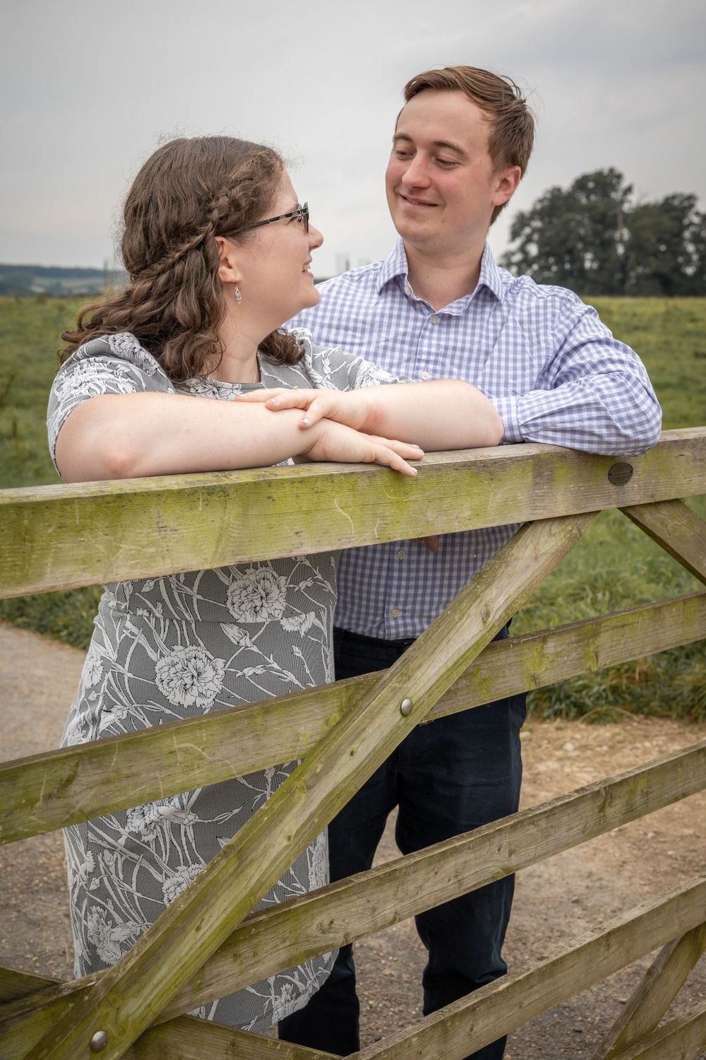 A couple shares a tender moment while leaning on a wooden gate in a countryside setting. Calke Abbey.