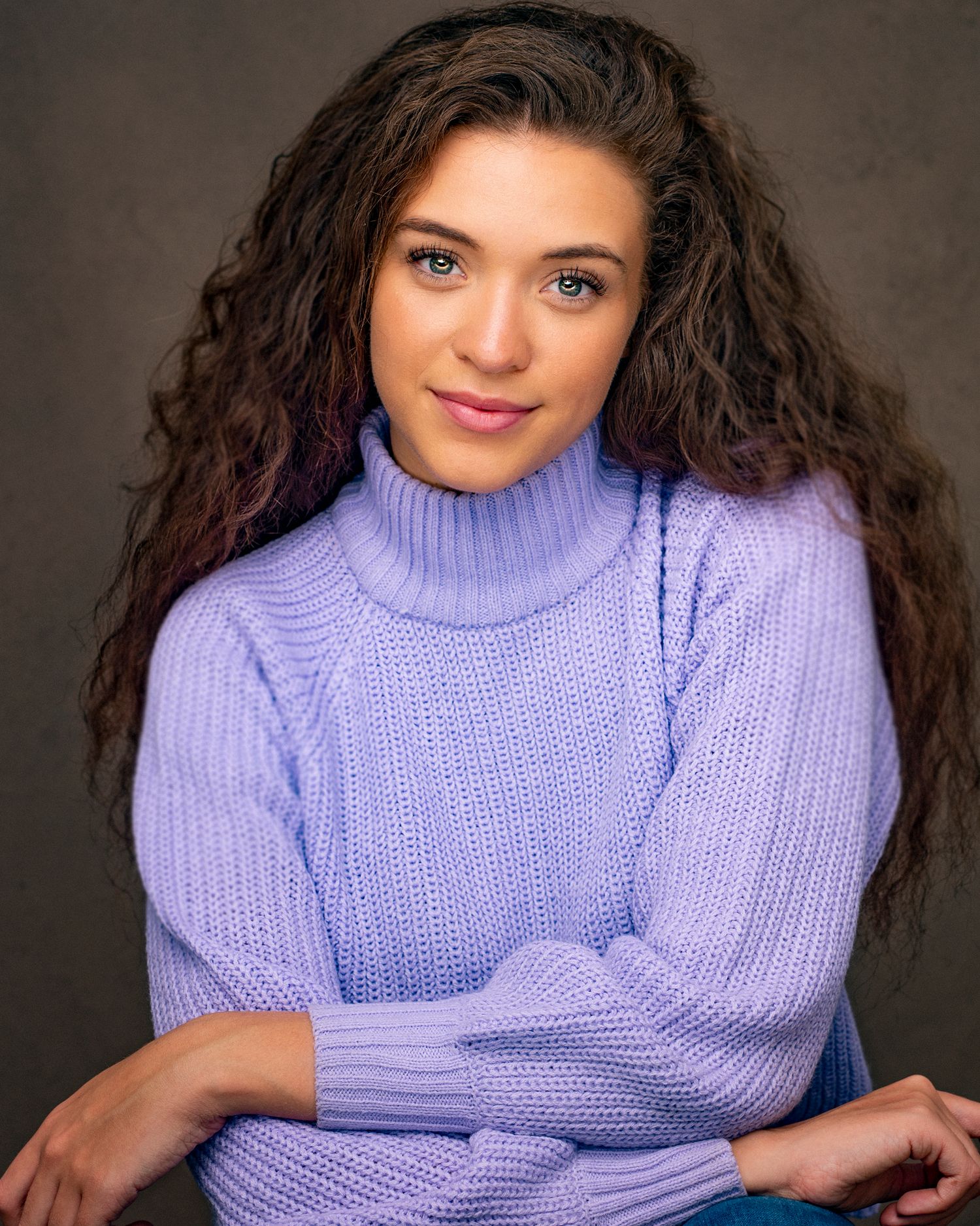 Professional headshot featuring a model in a lavender turtleneck sweater with curly hair.