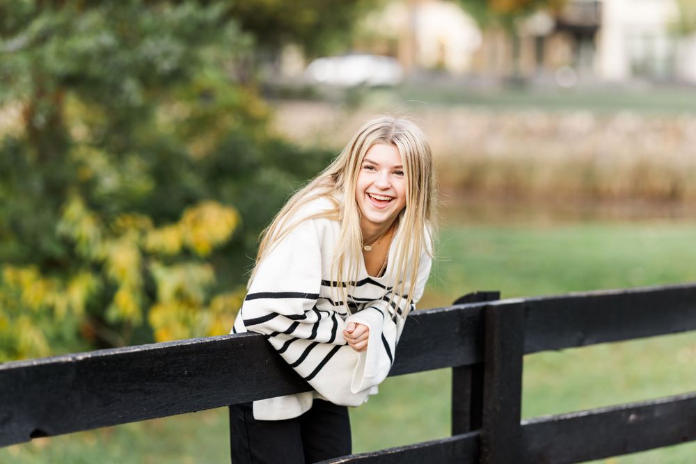 A person in a striped sweater leaning on a wooden railing and smiling outdoors.