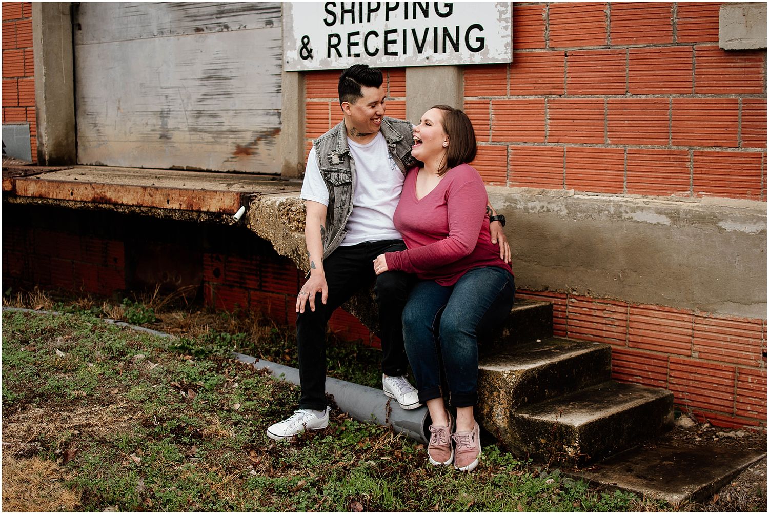 Couple sitting on concrete steps near shipping and receiving sign against brick building.