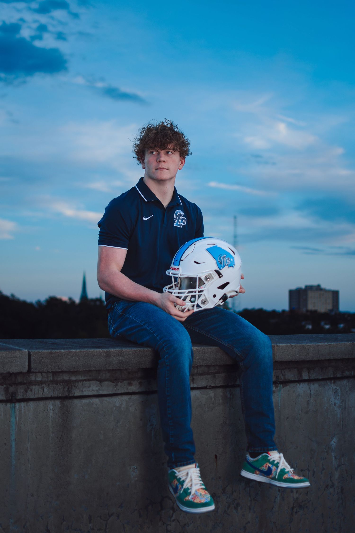 An athlete poses with a football helmet against a dusky blue sky.
