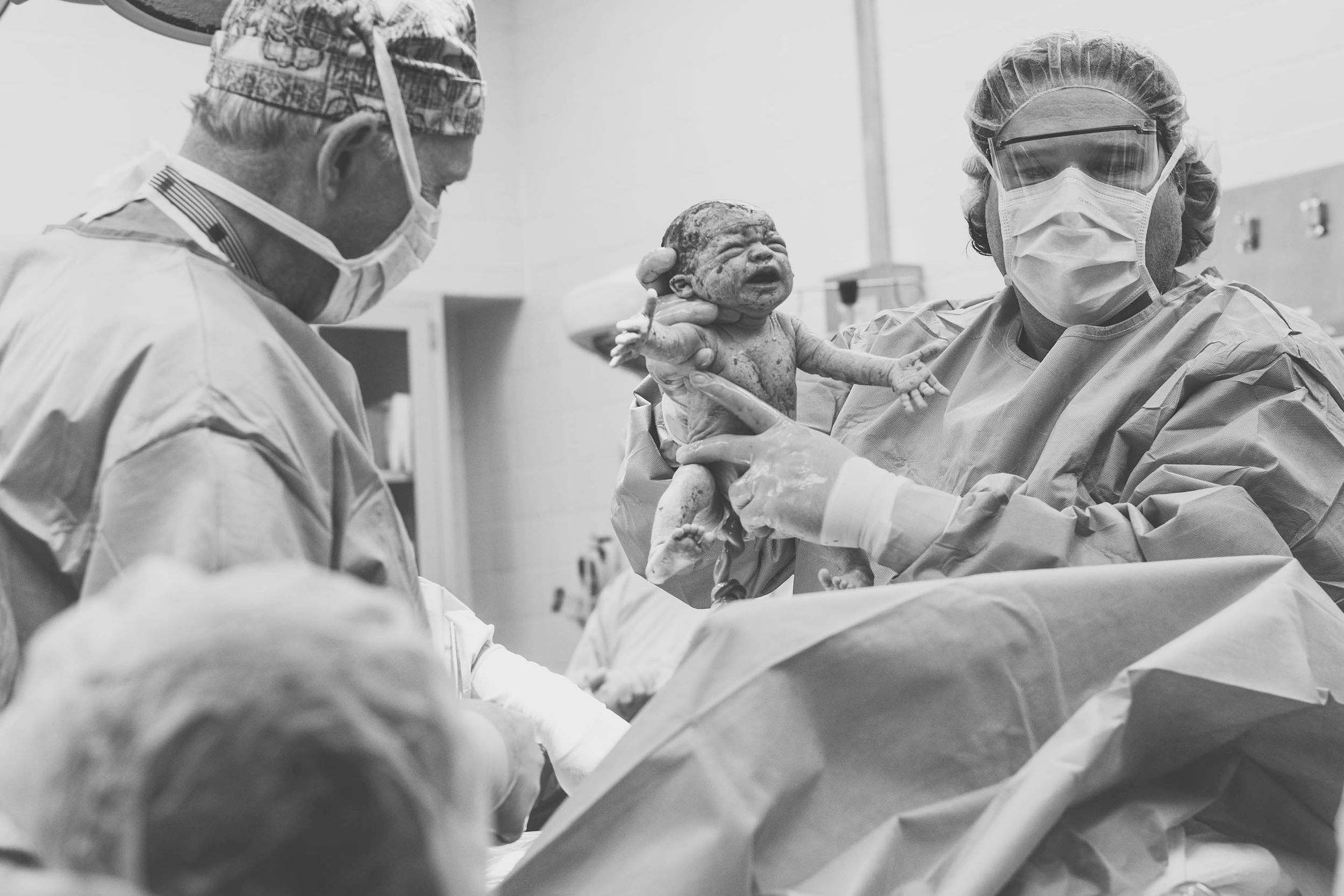 A doctor holding up a baby from a cesarean delivery for the parents to see