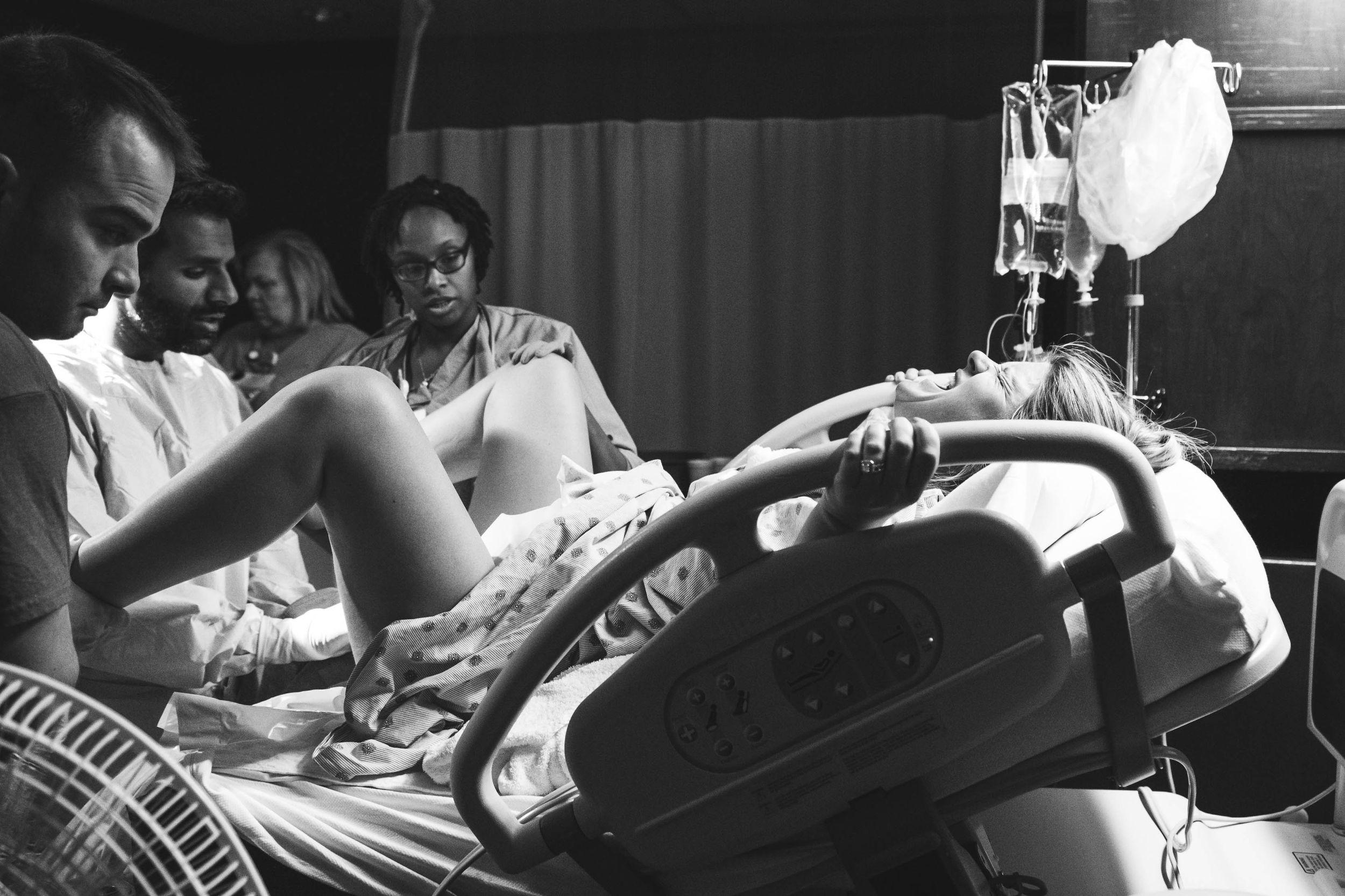 A person giving birth lying in a hospital bed while screaming and the medical staff preparing to catch the baby