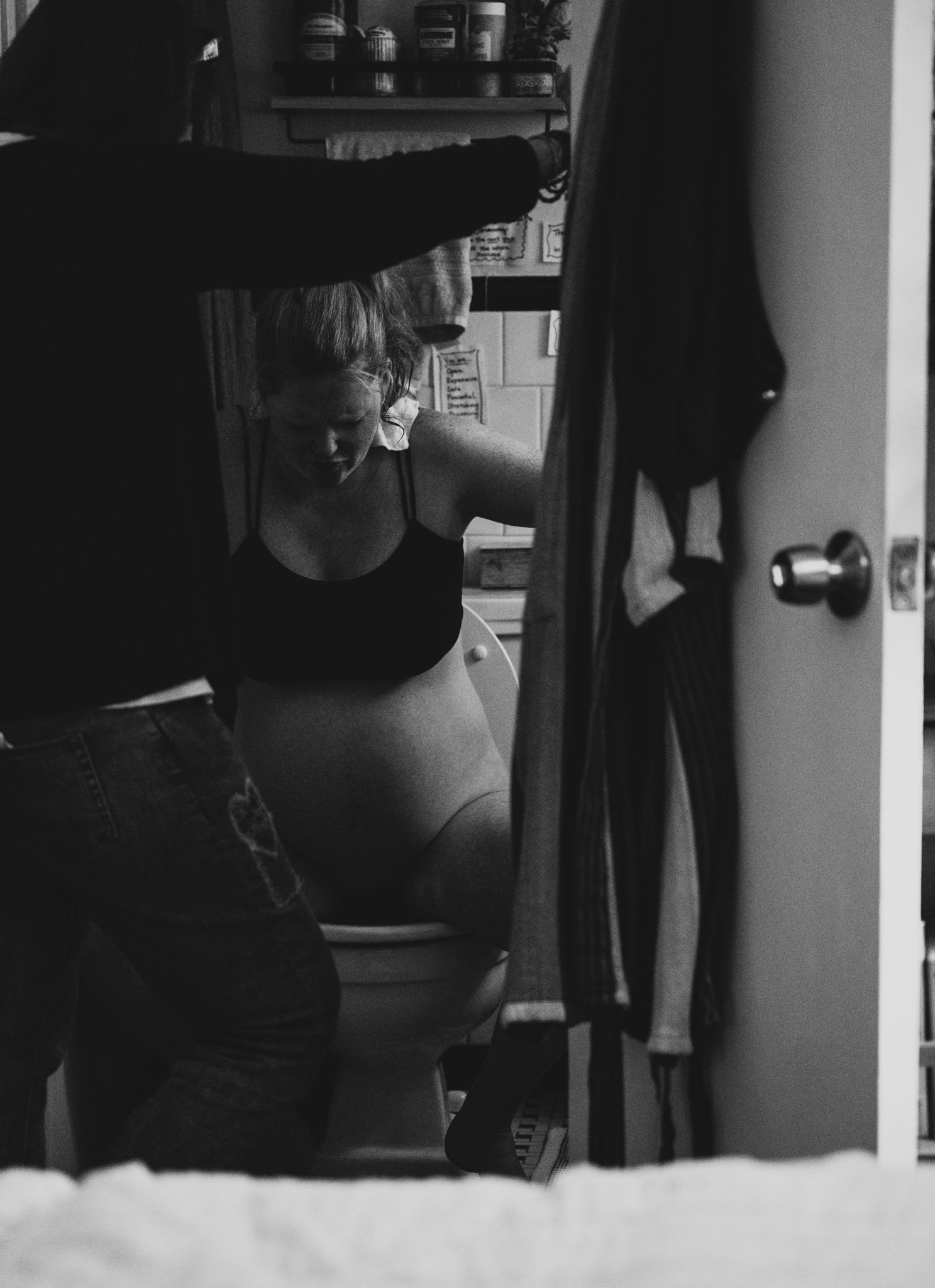 A person focused and laboring on a toilet as her midwife looks on