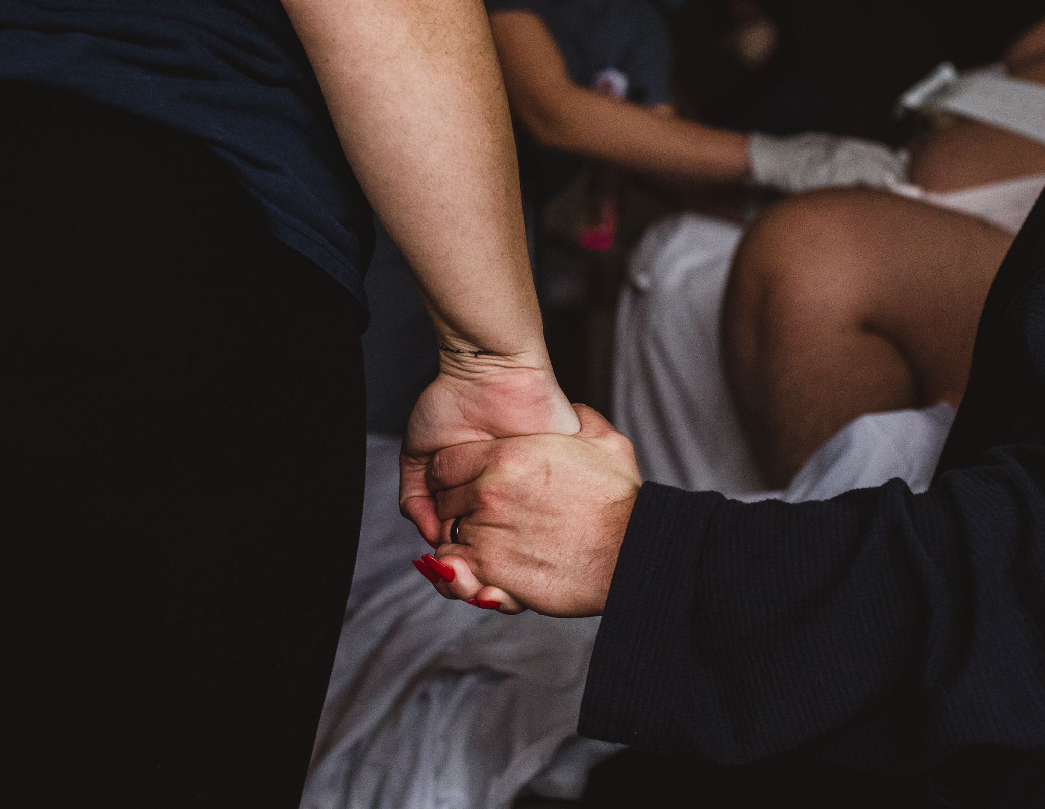 Two people's hands holding with a person giving birth in the background