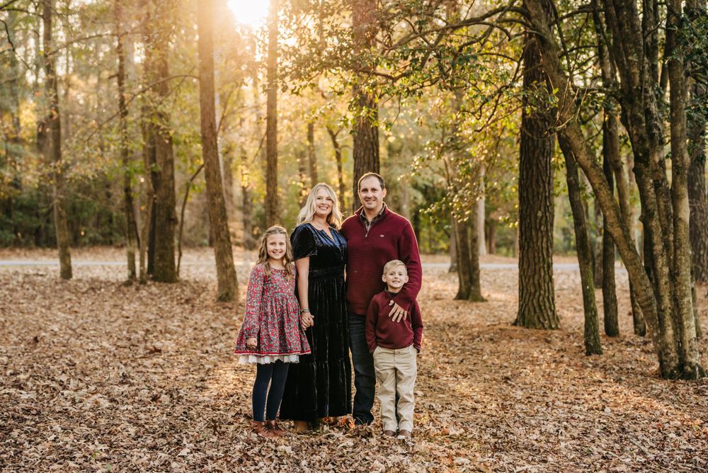 Family portrait in autumn forest with golden sunlight filtering through trees.