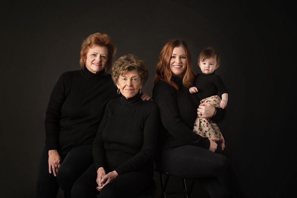 Elegant generational portrait with four people dressed in black against dark background.