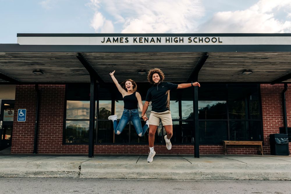 Two students jumping in celebration outside James Lenah High School entrance.