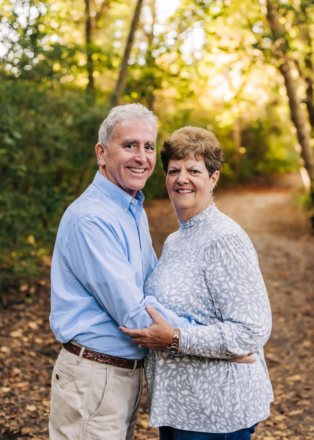 Mature couple embracing outdoors on autumn path with golden sunlight filtering through trees.
