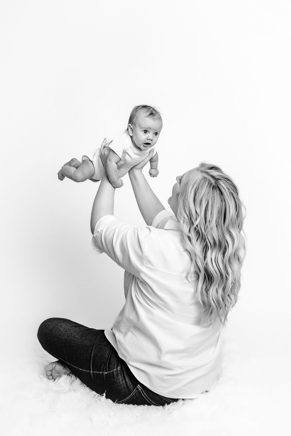 Black and white portrait of parent lifting baby in playful moment on white backdrop.