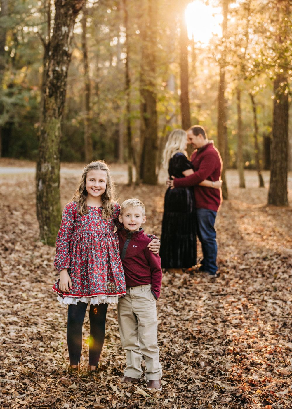 Family photo session in a sunlit autumn forest with fallen leaves covering the ground.