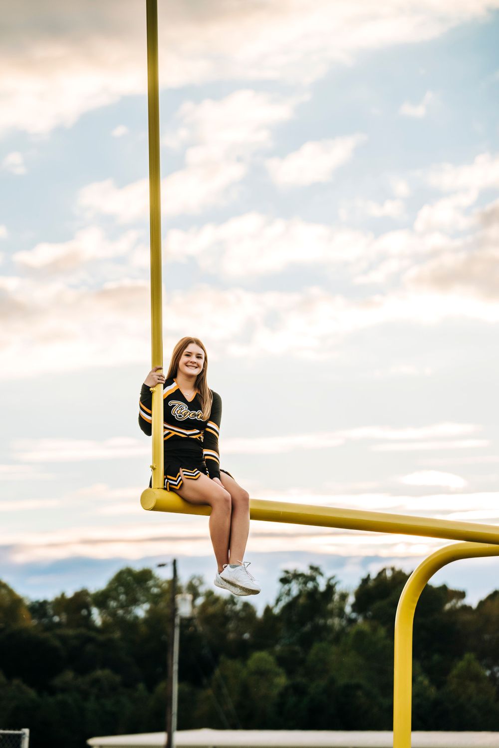 Student sitting on yellow goal post against cloudy sky at sunset.