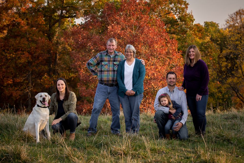 Fall family portrait with dog against colorful autumn foliage backdrop.
