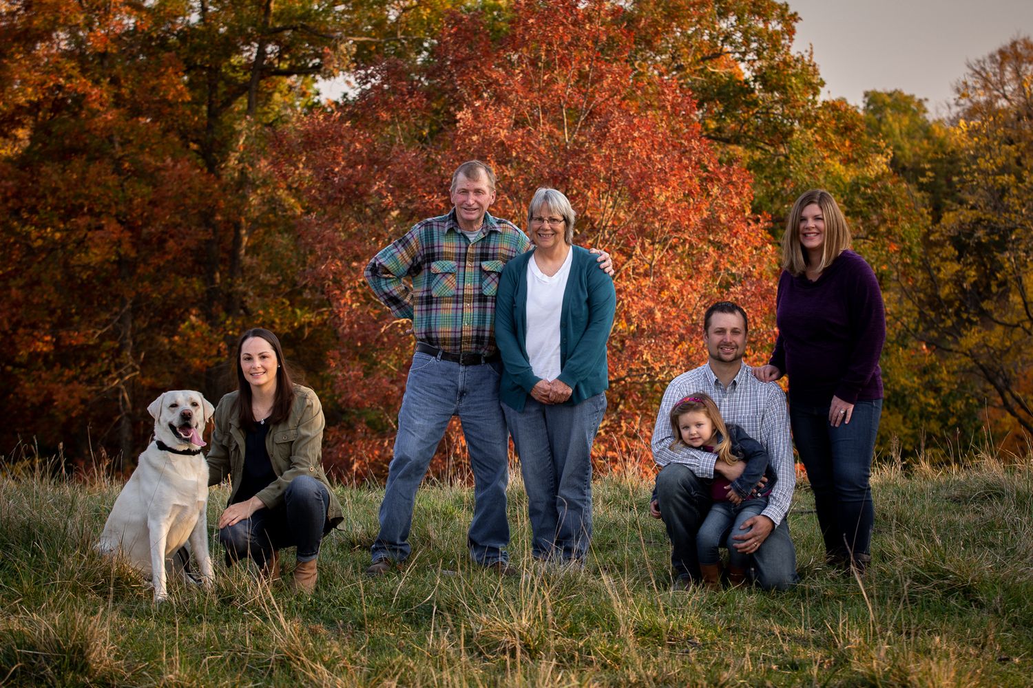Fall family portrait with dog against colorful autumn foliage backdrop.