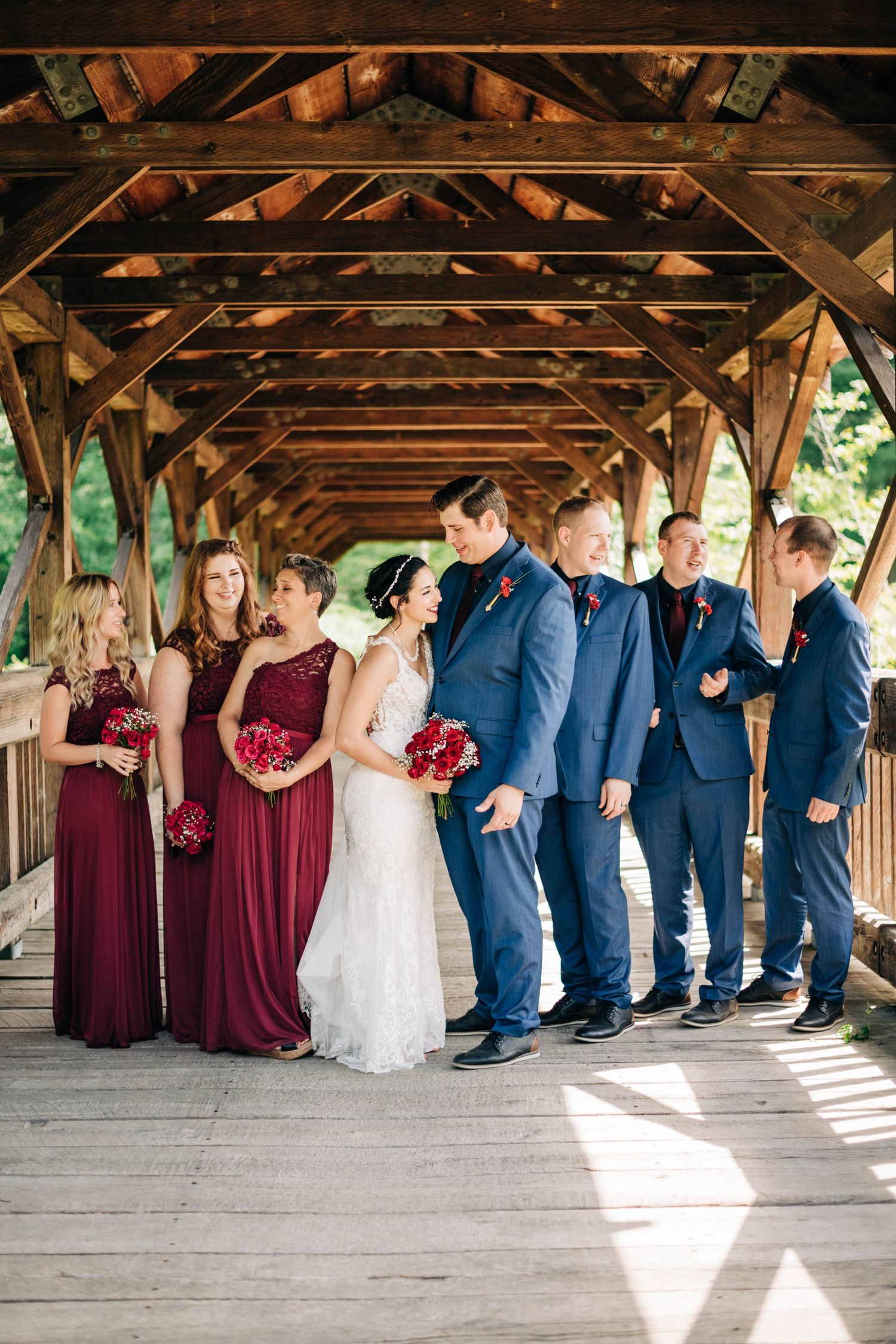 bridal party laughing on a covered bridge. bridesmaids in maroon dresses, men in navy suits.
