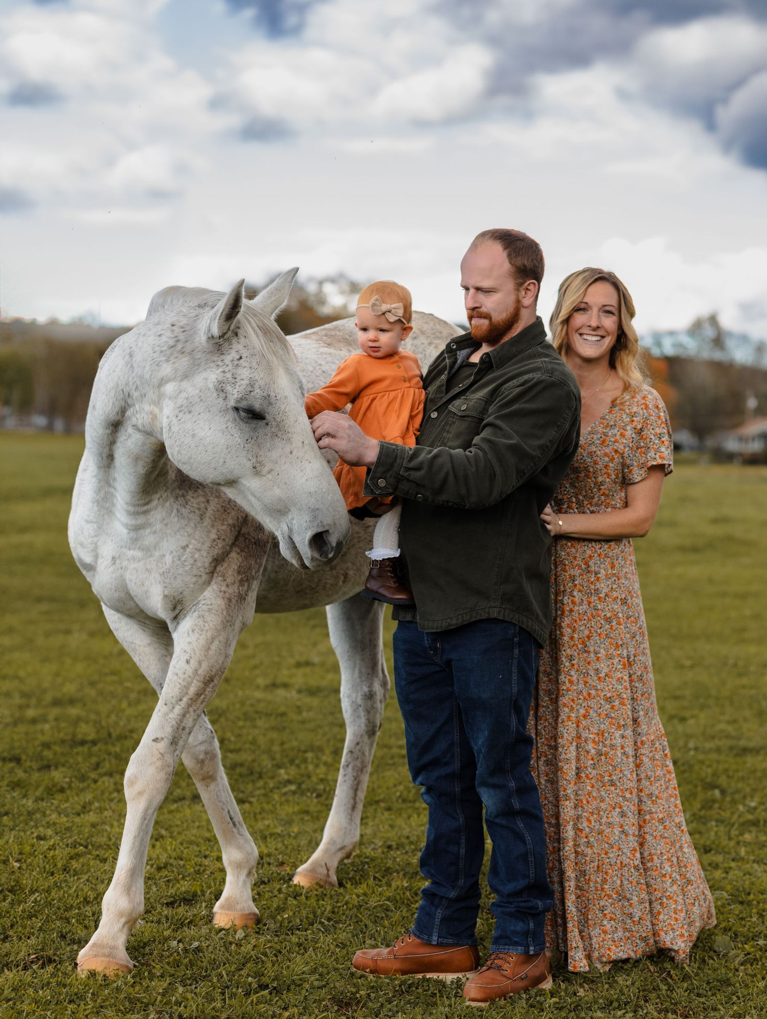 Family poses with white horse in green pasture during fall photo session.