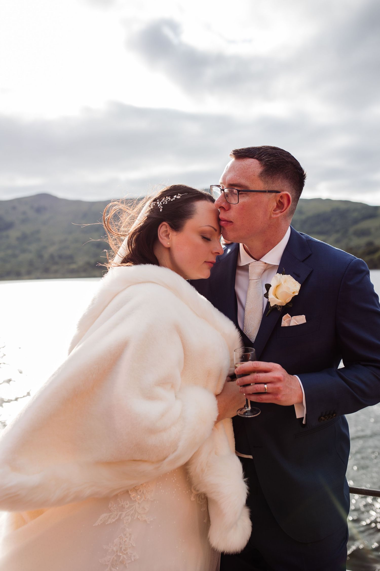 A tender moment shared during a lakeside wedding celebration on a cloudy day.